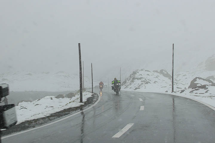 Flüelapass: kaksi moottoripyöräilijää räntäsateessa, sumua, lunta ja lampi